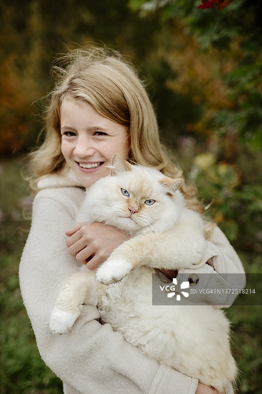 快乐的金发女孩在花园里抱着布偶猫图片素材