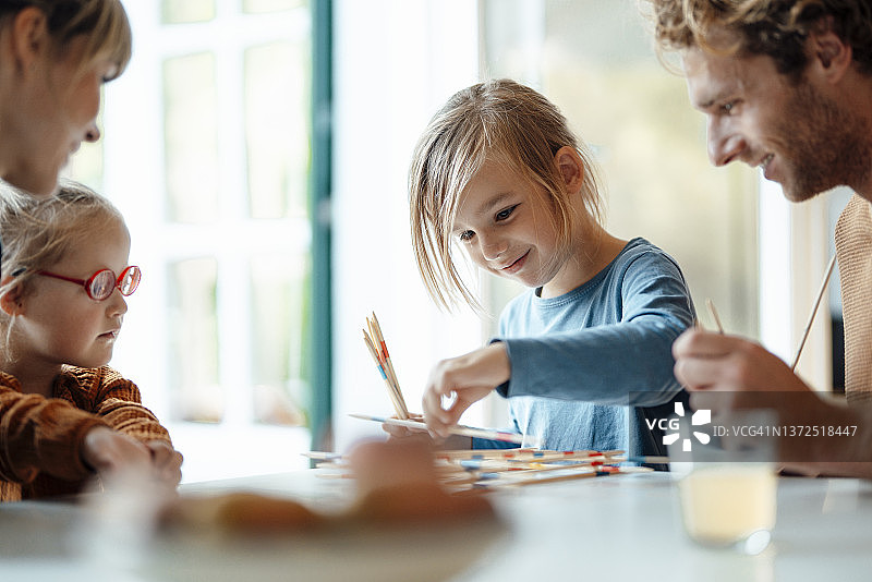 父母和姐姐看着男孩在家玩米卡多游戏图片素材