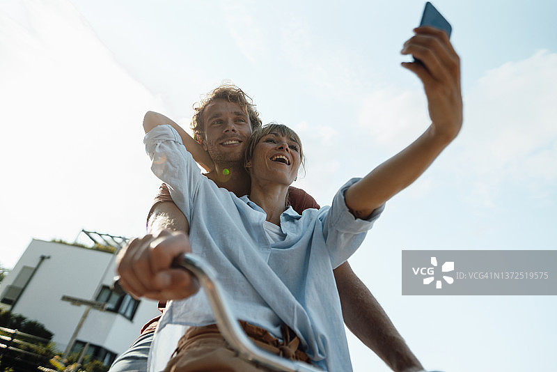 快乐的夫妇骑自行车用智能手机自拍图片素材