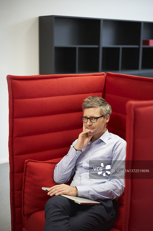 在办公室红色椅子上使用笔记本电脑的沉思的商人图片素材