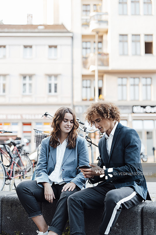 商务人士在智能手机上与坐在墙上的女商人交谈图片素材