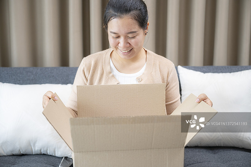 微笑女人坐在家里的沙发上打开纸板箱图片素材