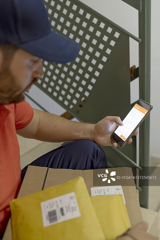 送货男人坐在包裹旁，用智能手机查看和更新订单图片素材