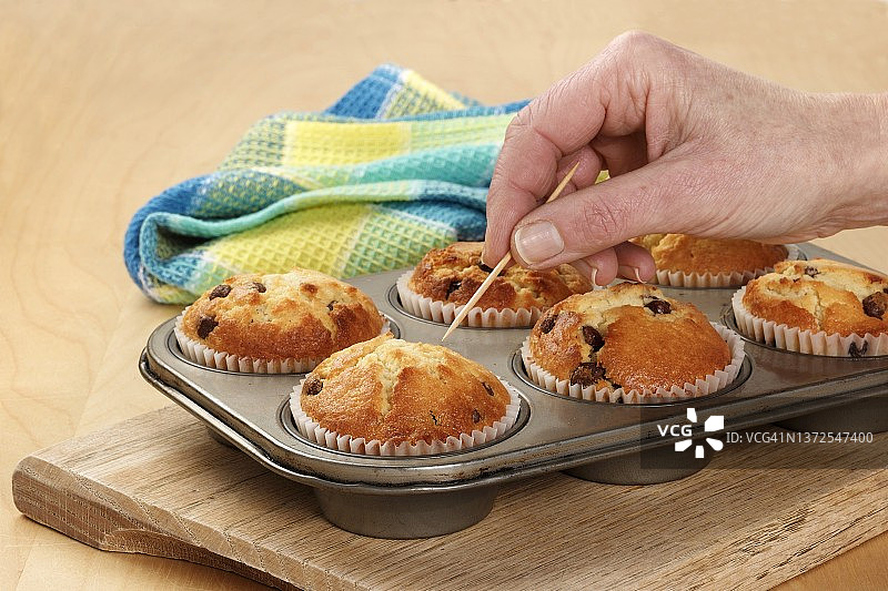 有人用牙签测试烤盘中的纸杯蛋糕是否完全烤熟图片素材