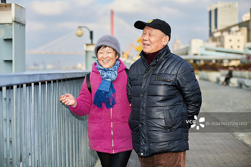 一对中国老年夫妇在河边的人行道上眺望远方，愉快地交谈着图片素材