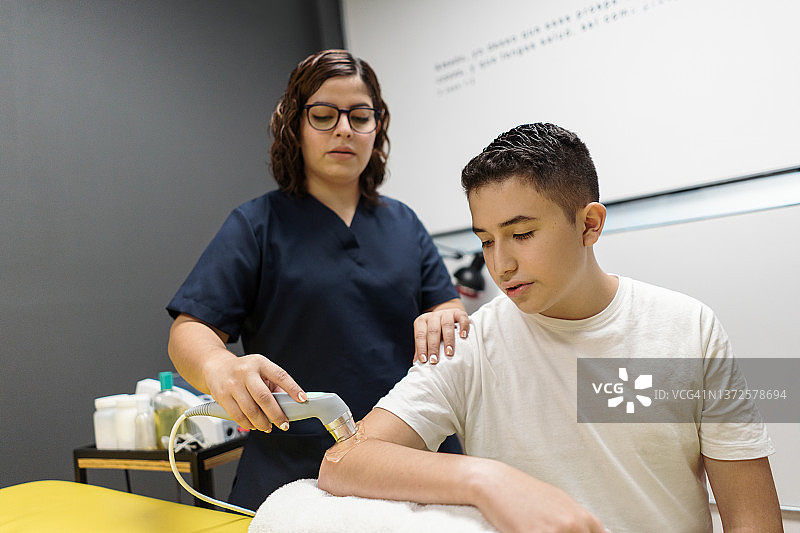 理疗师在青少年手臂上使用治疗设备图片素材