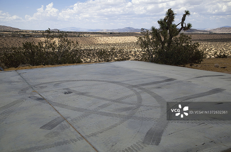 混凝土板上的轮胎痕迹；远处的沙漠植物山脉和蓝天白云图片素材