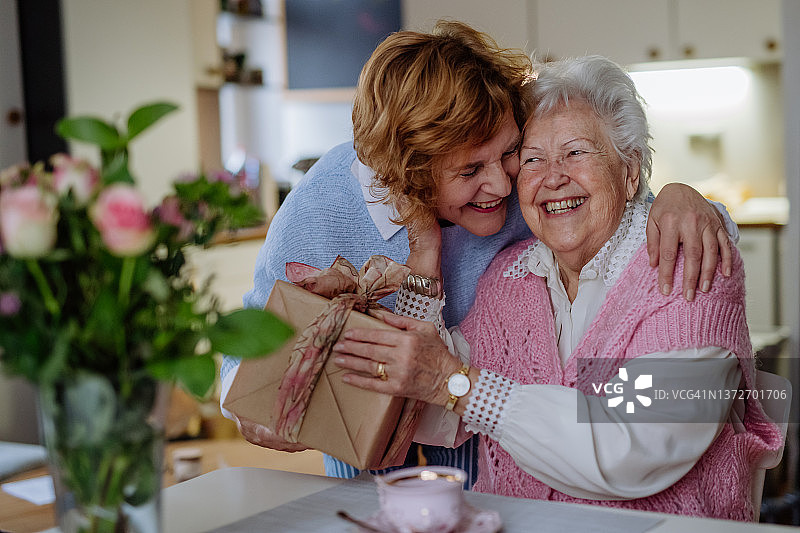 快乐的老年母亲在家收到成年女儿的礼物，母亲节概念图片素材