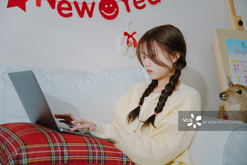 在阳光明媚的日子里，在沙发上用电脑工作的亚洲女孩图片素材