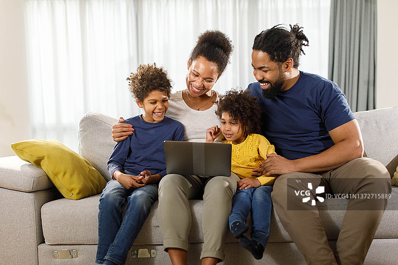 快乐的黑人家庭在家里的沙发上使用笔记本电脑。图片素材
