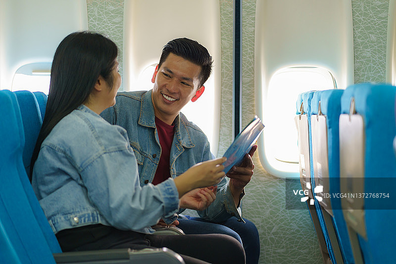 亚洲情侣在飞机客舱座位上看地图讨论目的地，航空旅行服务概念图片素材