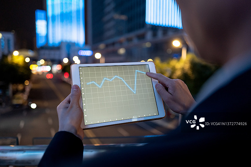 在夜晚的城市街道上使用平板电脑的男商人图片素材