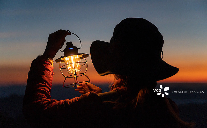 女子在黄昏时分点亮电灯，欣赏美丽的自然暮光剪影图片素材