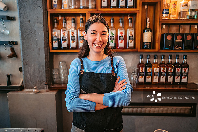 年轻微笑的咖啡师在吧台后，双臂交叉图片素材