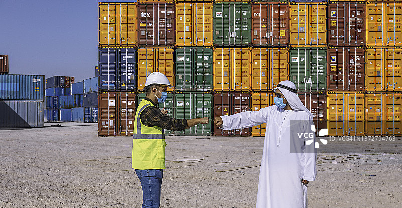 疫情期间阿拉伯商人和工程师在大型商业码头上戴着口罩，互相用手肘打招呼图片素材