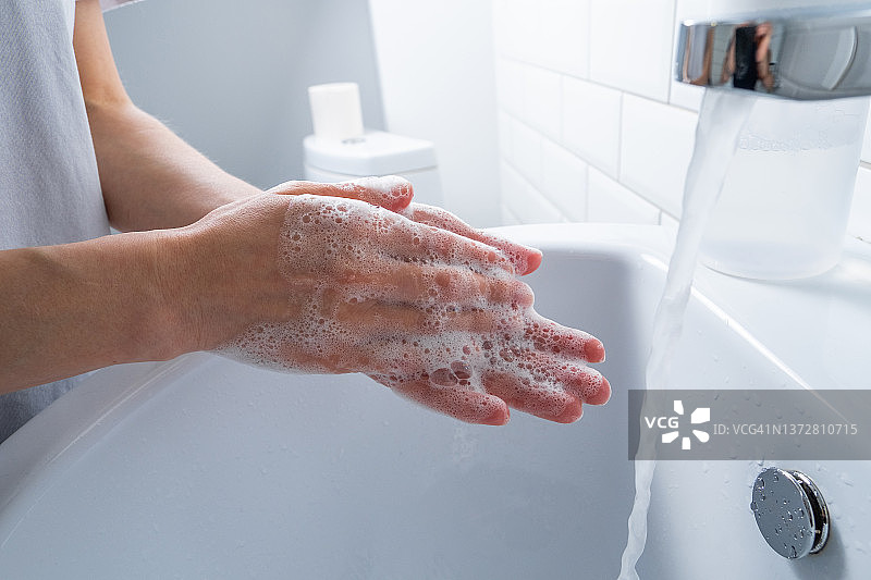 一名妇女在浴室、家中或公共场所用肥皂洗手消毒，预防疾病，讲究卫生。卫生概念，使用非接触式给皂机，遵守疫情和冠状病毒措施。图片素材