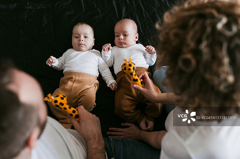 父母拿着玩具，双胞胎在床上休息图片素材