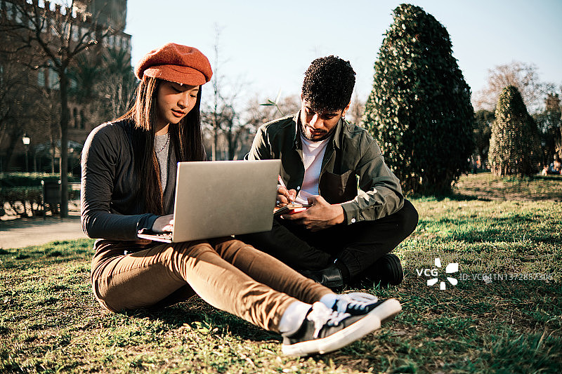 两位大学生坐在大学校园的绿草地上一起学习图片素材