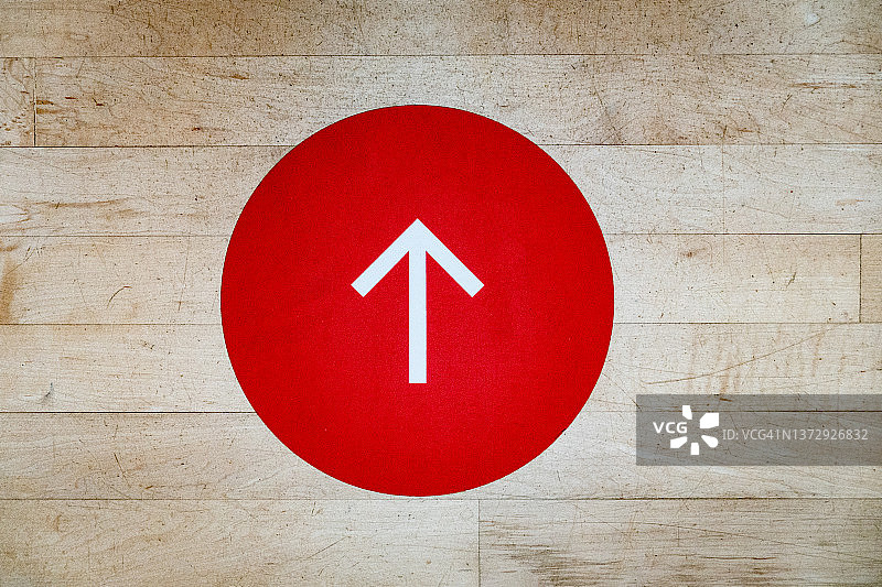 木地板上的红色圆圈中的白色箭头图片素材