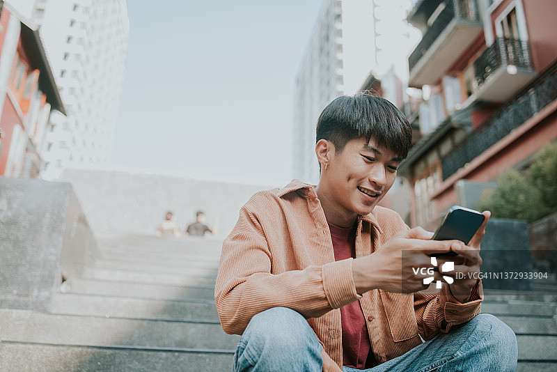 亚洲男大学生在手机上发短信。图片素材