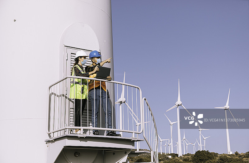 疫情期间在风力发电场作业的戴防护口罩的工程师图片素材