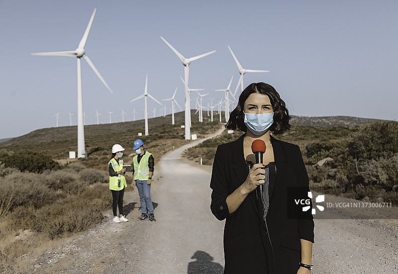戴着口罩的女电视新闻记者在大流行期间报道可再生能源图片素材