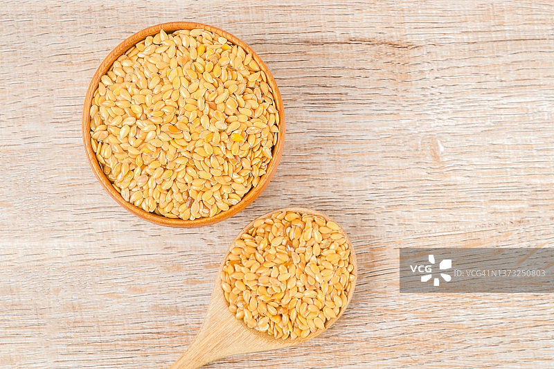 木桌背景上，木碗中盛放的金色亚麻籽与木勺的俯视图图片素材
