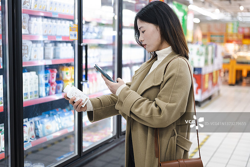 年轻亚洲女性在超市用手机扫描产品条形码，查看产品信息图片素材