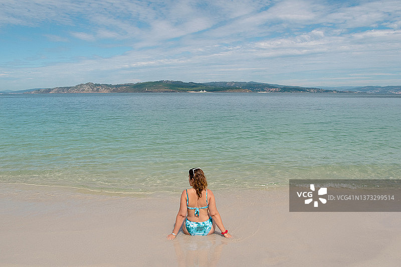 西班牙海滩上，穿着比基尼坐在水边的女子背影图片素材
