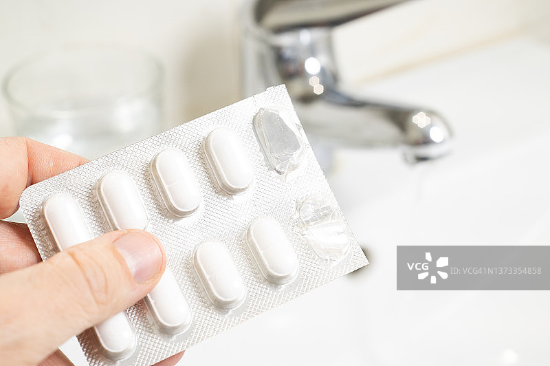 一个男人在水龙头旁吞下一粒胶囊药丸图片素材