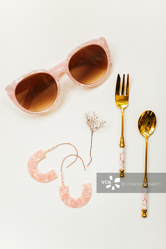 白色纸上的粉色灵感搭配：太阳镜、耳环、勺子、刀和干燥植物图片素材