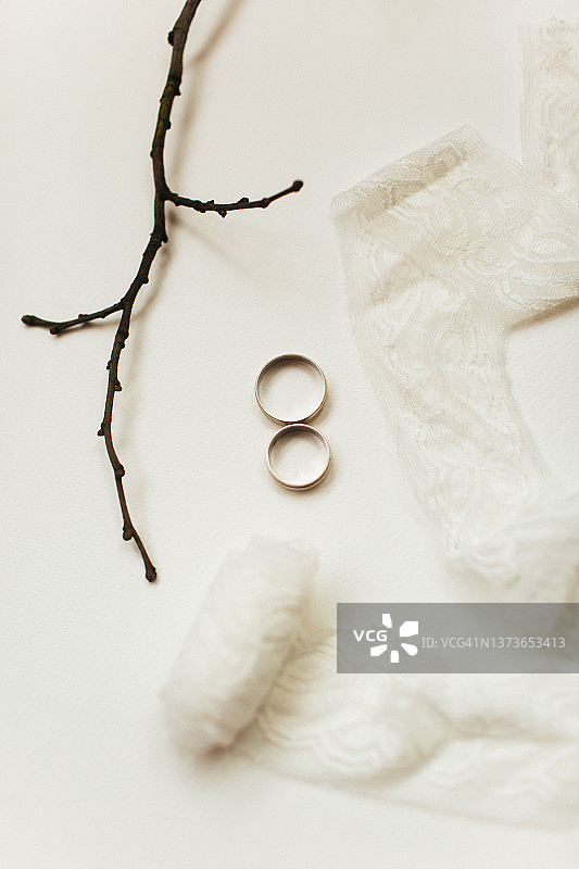 白色纸张上的结婚戒指、蕾丝带和树枝图片素材