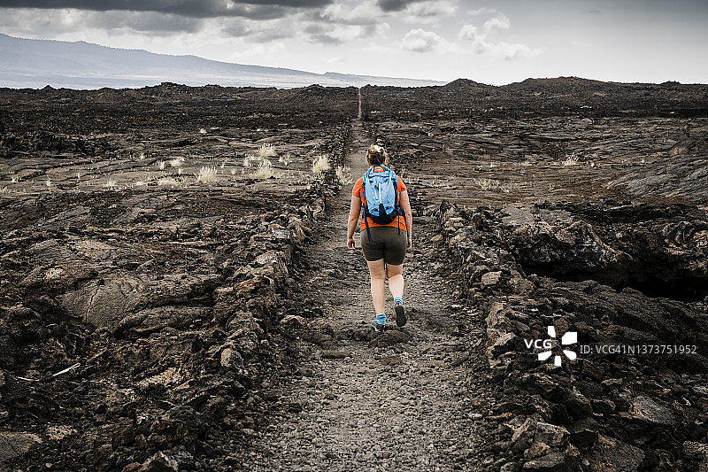 在夏威夷偏远的熔岩地中沿着笔直小路远足的女人图片素材