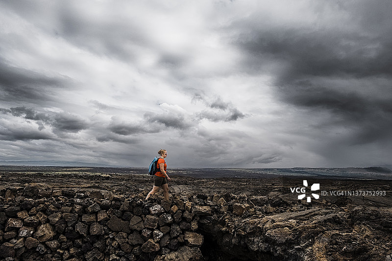 女子在偏远的熔岩地带徒步，头顶是戏剧性的暴风云图片素材
