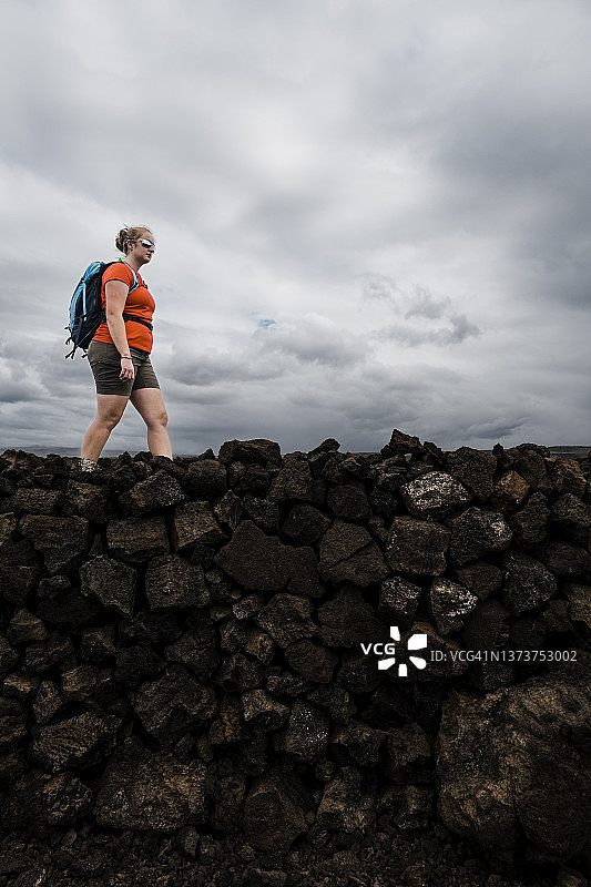 女子在偏远的熔岩地带徒步，头顶是戏剧性的暴风云图片素材
