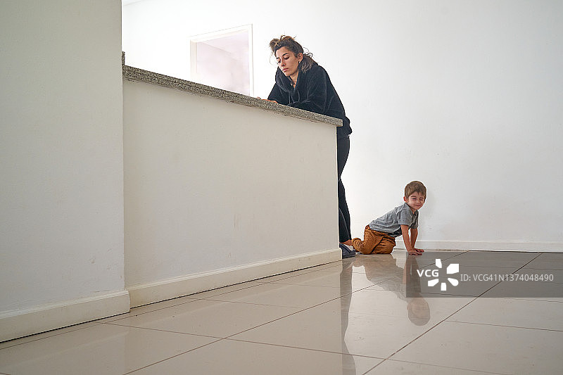 在厨房玩耍、妈妈在看手机的男孩图片素材