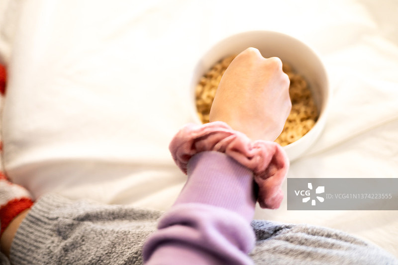 混血少女在床上享用干麦片零食，手腕上戴着发圈图片素材