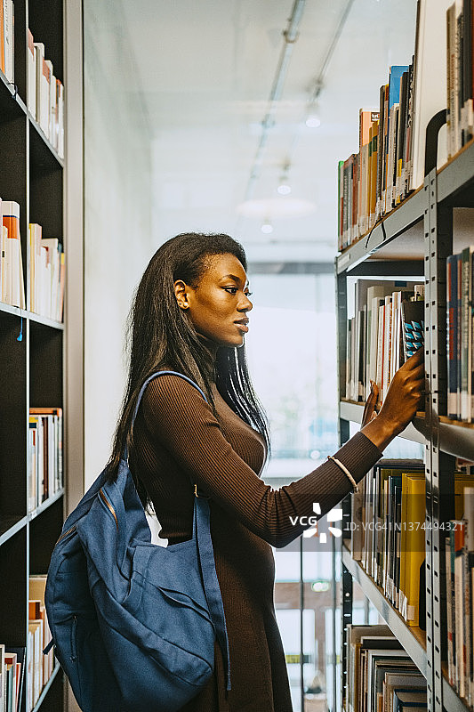 年轻女子在图书馆背着背包找书侧视图图片素材