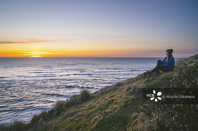 日落时分，一位女性坐在海边悬崖上图片素材