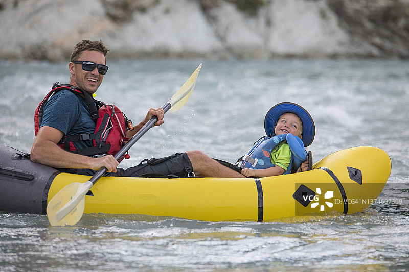 父子在河上划充气筏，穿着救生衣。图片素材