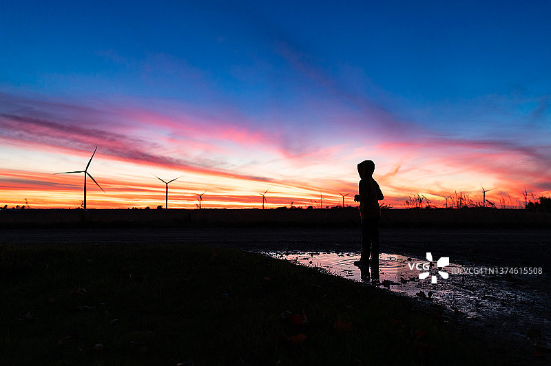 日落时分风力发电场水坑中男孩的轮廓图片素材