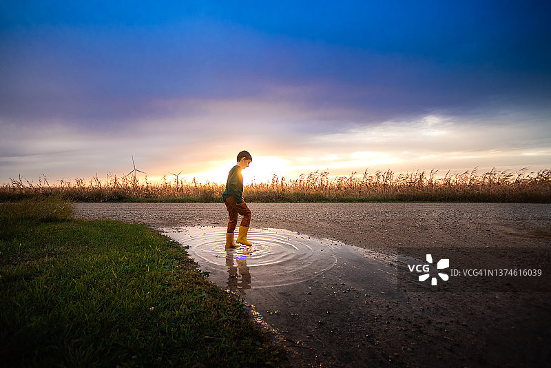 男孩在日落时分的碎石路上玩水图片素材
