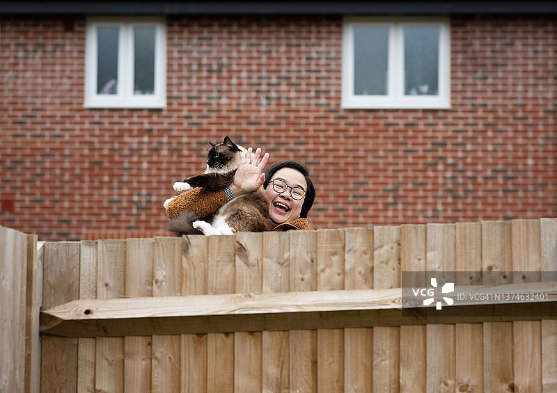 快乐的邻居在花园里隔着栅栏和她的猫挥手图片素材