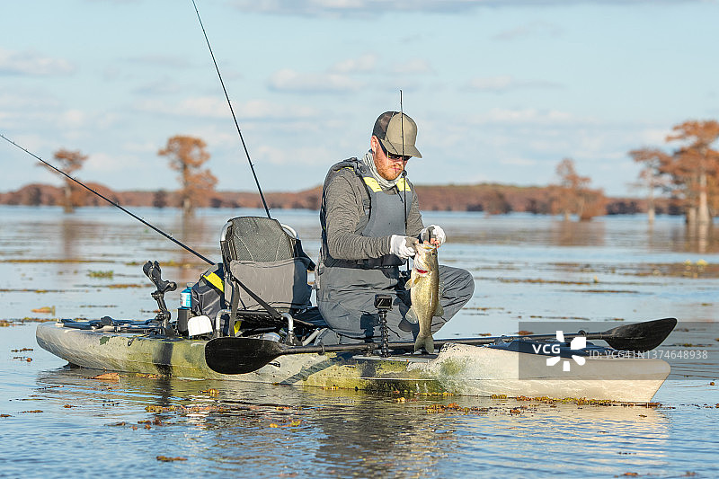 男子在皮划艇上钓起大口黑鲈鱼图片素材