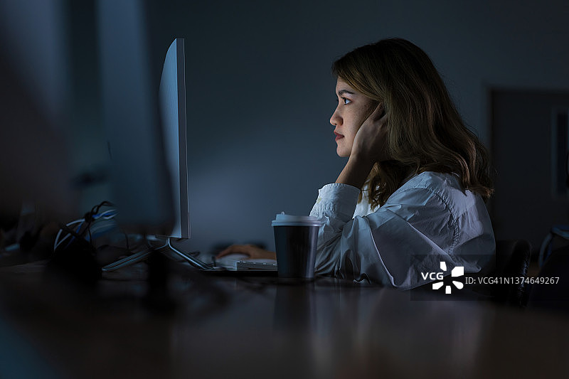 疲惫的年轻亚洲女性在工作办公室中心熬夜，她正在使用台式电脑，承受着压力和截止日期的概念图片素材
