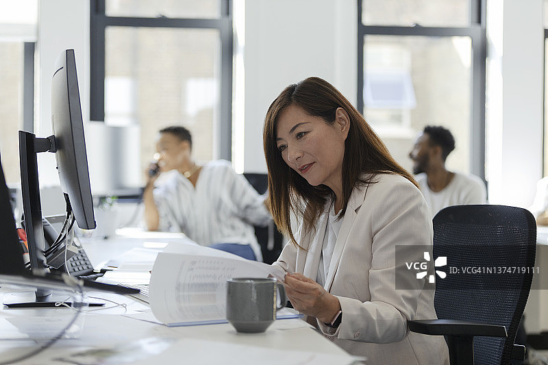 女商人审查开放式办公室办公桌上的文件图片素材