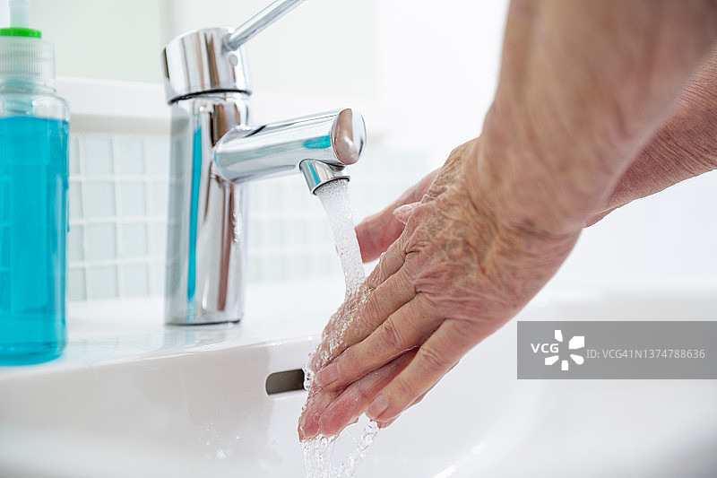 靠近在浴室水槽洗手的老年妇女图片素材