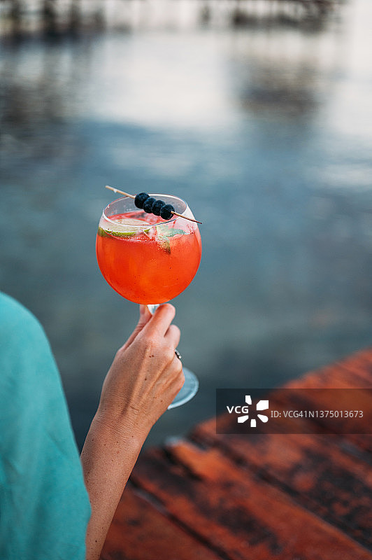 女人手持一杯红色鸡尾酒站在木制码头上图片素材