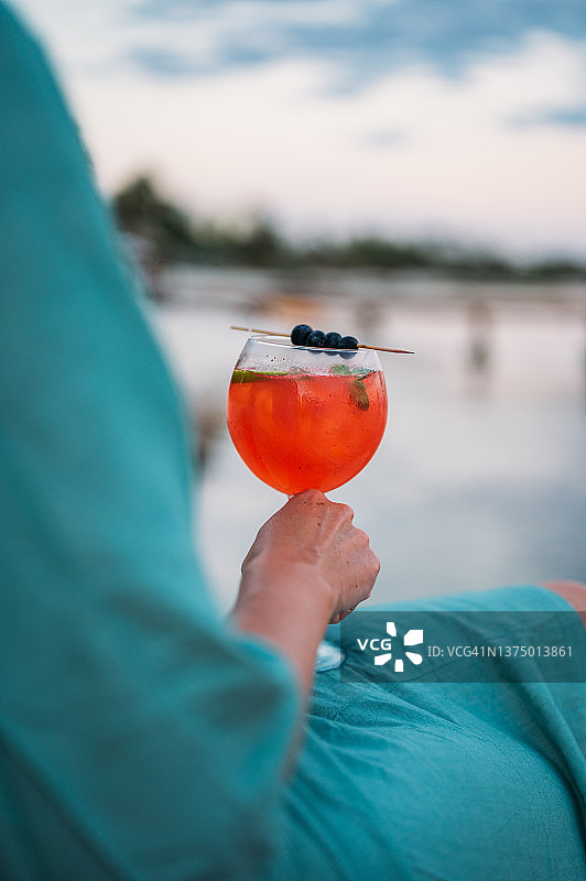 女人手持一杯红色鸡尾酒站在木制码头上图片素材