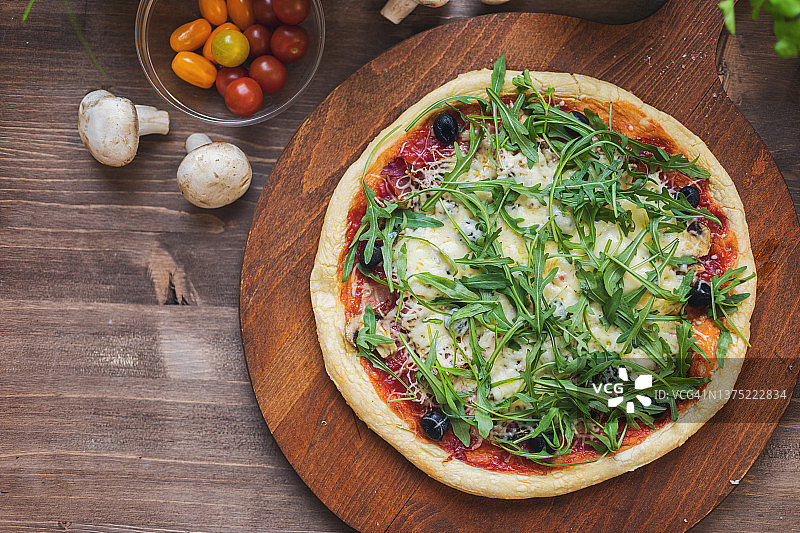 新鲜出炉的自制意式火腿芝麻菜披萨，配有橄榄和马苏里拉奶酪图片素材